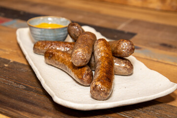 A plate of delicious sausages and a little pot of mustard on a wooden kitchen work top