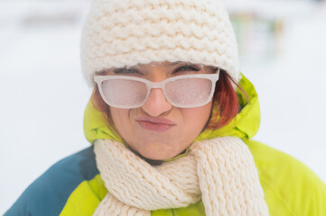 Portrait of a woman in glasses covered with hoarfrost. Upset girl freezing in very cold weather...
