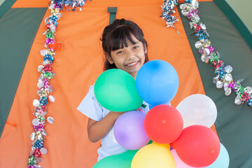 Fototapeta na wymiar Asian little girl smiling and holding a bunch of balloons for festival decorations.
