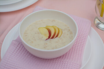 Oatmeal with apple for breakfast. Healthy eating. A useful breakfast. Porridge in a white ceramic cup on a pink tablecloth.
