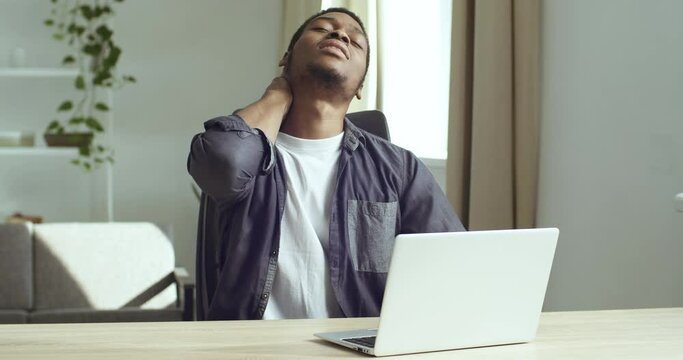 African business manager man freelancer working at laptop sitting at desk feeling pain in neck suffers from spinal spasm injuries uncomfortable posture feels fatigue overwork in workplace office home