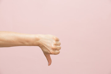 Female caucasian hand shows thumb down gesture, on pink background. Minimal concept. Copy space