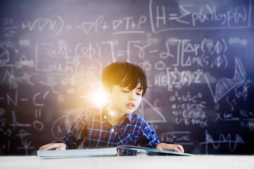 Smart little boy reading a textbook in classroom