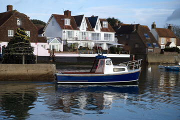 Fototapeta premium View of a local fishing boat leaving Emsworth Harbour with the Christmas Tree made of Lobster Pots in the background.