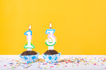 13 number candle on a cup cake with colorful sprinkles and yellow background thirteenth birthday anniversary celebrations