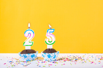 25 number candle on a cup cake with colorful sprinkles and yellow background twenty fifth silver jubilee birthday anniversary celebrations