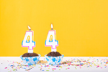44 number candle on a cup cake with colorful sprinkles and yellow background forty fourth birthday anniversary celebrations