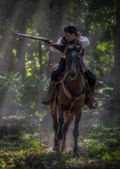 Cowboy is riding a horse and holding a long gun in his hand, ready for shooting.