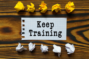 Fototapeta premium On a wooden board lie crumpled leaves of paper and a sheet from a notebook on which it is written - Keep Training