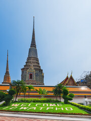 Fototapeta na wymiar Wat Pho public ancient temple in Bangkok, Thailand. Thai architecture beautiful view, mosaic chedi and temple buildings at entrance under blue sky. Welcome to Wat Pho lettering on green lawn