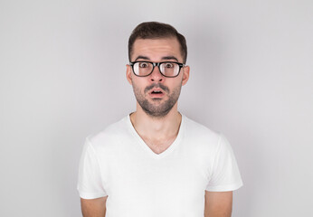 Surprised man in eyeglasses wearing white undershirt over grey background