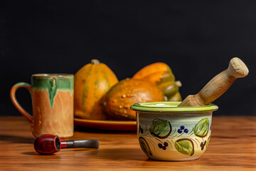 Still life of a mortar, smoking pipe, mug and pumpkins. Wood and black background.