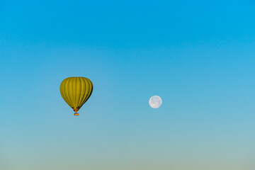 Hot air balloon flying over Cappadocia with full moon, in blue sky