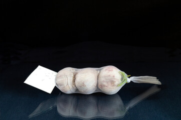 The Garlic in net rests upon glass table with reflection.