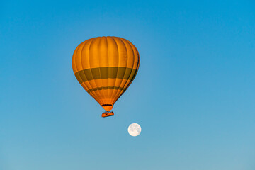 Hot air balloon flying over Cappadocia with full moon, in blue sky