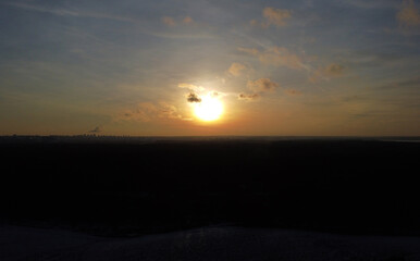 Big sun over the silhouette of black forest trees at sunset
