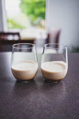 couple of espresso martinis in wine glasses on kitchen counter with dining room bokeh