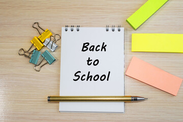 back to school is written on a notebook that lies on a wooden table among paper stickers and stationery clips. Concept photo