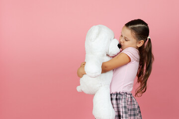 mock up girl with ponytails and pink dress hugs and kisses white teddy bear isolated on pink background.