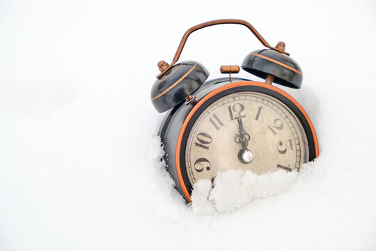 Old retro alarm clock in winter in snow on white background shows twelve hours.