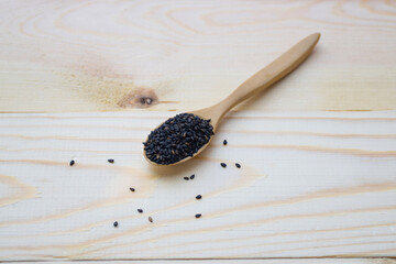 Black sesame seeds in wooden spoon pile on wood table