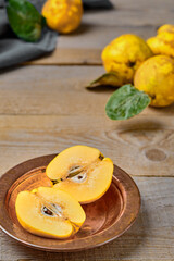 Fresh ripe quince fruits cut into halves on a metal plate. Close-up, rustic wooden table. Healthy organic yellow quince fruits.