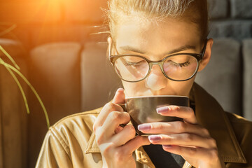 Young woman drinking coffee cup and sitting in cafe. Girl in glasses pauses after work.