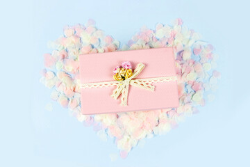 Beautiful pink gift box on heart made of pastel paper confetti and blue background. Valentine's Day, wedding, love concept. Top view, flat lay, copy space.