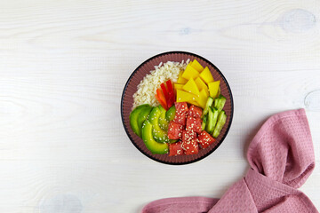 Poke bowl with salmon, rice, avocado, cucumber, mango, pepper and sesame seeds on a white wooden background.  Asian trendy, diet food. Top view. Flat lay. 