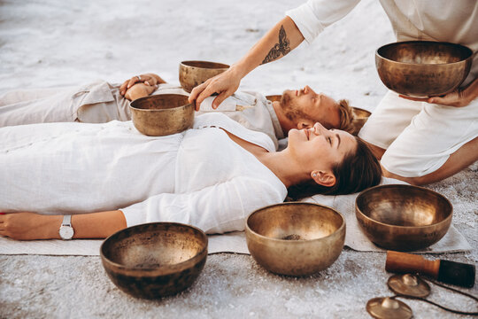 group therapy with Tibetan singing bowls for a girl and a boy lying on the ground in the middle of the desert surrounded by copper bowls, meditation and relaxation