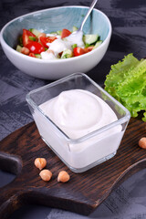 Vegan chickpea mayonnaise made of aquafaba in a glass bowl and salad with fresh vegetables on the grey table. Salad dressing