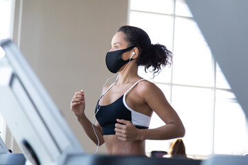 Fototapeta na wymiar Sports hispanic woman training on treadmill in gym and wearing face mask against coronavirus during global pandemic of covid-19 virus