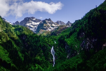 big waterfall in the mountains with green trees and a mountain with snow