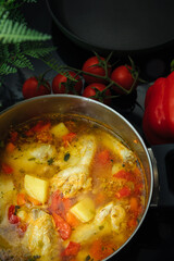 Soup with poultry, potatoes and greenery. Tomatoes and peppers next to a saucepan with soup