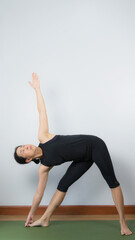 Asian young woman wear a black yoga outfit . Practicing yoga Standing Asanas Action UTTHITA TRIKONASANA (Extended triangle pose).Home yoga practice on white background