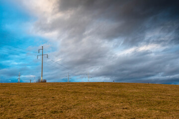 Obraz premium Wide angle view, electricity pylons on lifeless hill , dramatic gathering clouds.