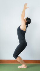 Asian young woman wear a black yoga outfit . Practicing yoga Standing Asanas Action UKTASANA (Fiera pose) .Home yoga practice on white background