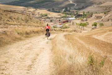 a pilgrim women cycling a dirt road entering Hontanas village, province of Burgos, Castile and Leon, Spain