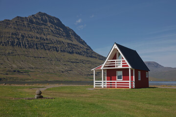 Traditional red painted wooden panel house with mighty Holmatindur mountain in the background in Eskifjordur, East Iceland © Jiri Vondrous