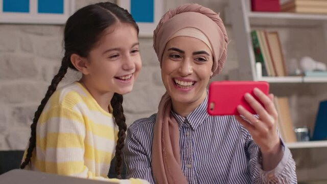 My mother is having a video call with her daughter on the phone.Mother dressed in hijab works at home. Working remotely.