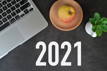 Flat lay view of laptop, apple and plant over black background written with number 2021. 