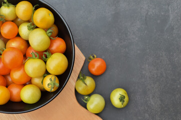 Top view and selective focus of fresh cherry tomatoes or the scientific name called as Solanum lycopersicum in the black bowl with chopping board and over black background.