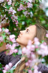 Fototapeta premium Beautiful young woman looks at a blooming apple tree in the park