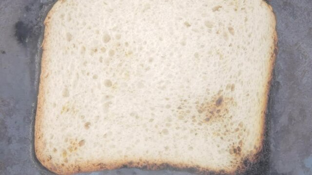 Timelapse overhead closeup shot: a piece of sliced bread in an old pan, cooking and burning until it's completely destroyed and reduced to black char.
