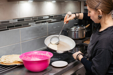 A teenage girl pours the pancake batter into a hot pan with a large spoon. Liquid pancake batter. Homemade pancakes.
