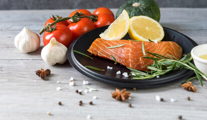 Grilled salmon steak on vintage wooden board with fork, olive oil, vegetables, herbs and spices on dark concrete background. Raw salmon fillet with vegetables, spices and lemon on wooden table.