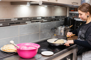 The young cook turns the pancake in the pan to the other side using the kitchen spatula. Homemade pancakes.