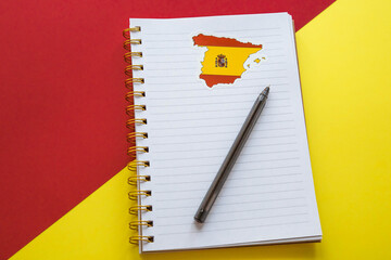 notebook with the spanish flag and pen on red-yellow backgroud
