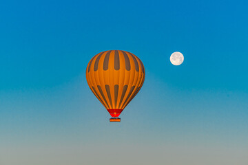 Hot air balloon flying over Cappadocia with full moon, in blue sky