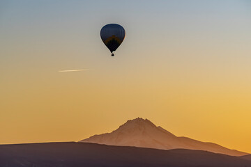 Hot air balloon rising in Cappadocia, with Erciyes mountain background. Orange color sky, An aircraft over Kayseri city